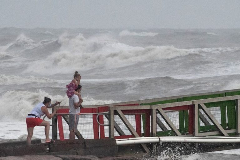 LYNXNPEG6O0IO.jpg,Foto del sábado de una niña cubriéndose la cara por los fuertes vientos mientras dos miembros de su familia observan el oleaje alto consecuencia del huracán Hanna en Galveston, Texas.
Jul 25, 2020. REUTERS/Adrees Latif; Crédito: ADREES LATIF, Reuters